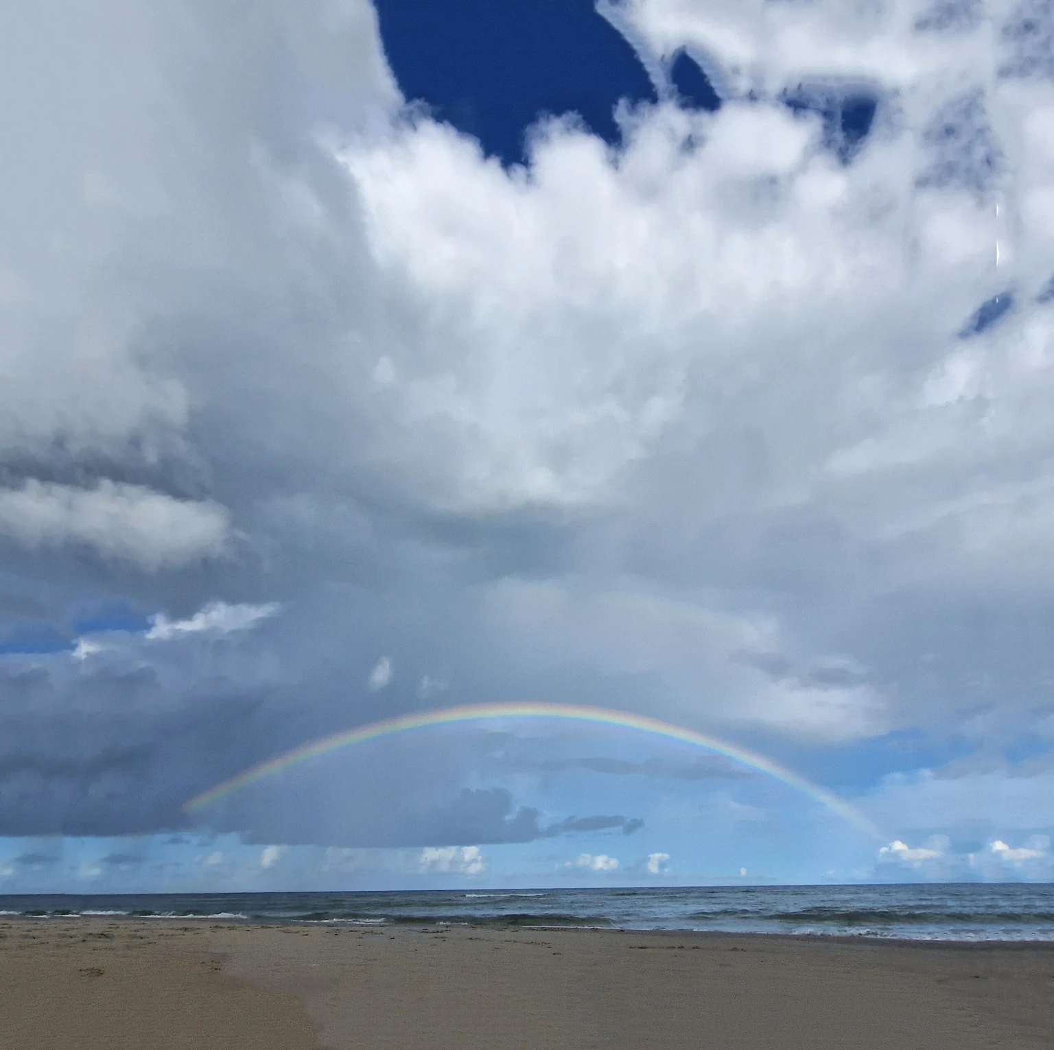 Regenbogen über dem Meer unter hohen Wolken